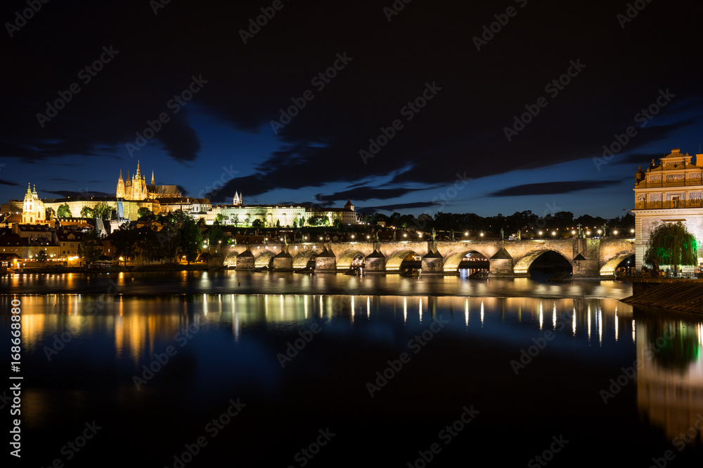 Obraz premium View of the lit Prague (Hradcany) Castle, Charles Bridge (Karluv most) and their reflections on the Vltava River in Prague, Czech Republic, at night.