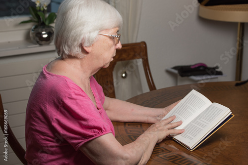 Old lady reading in her living room a book