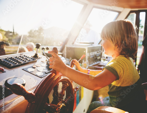 Cute little boy pretending to a be captain, child steering a ship at sunset photo