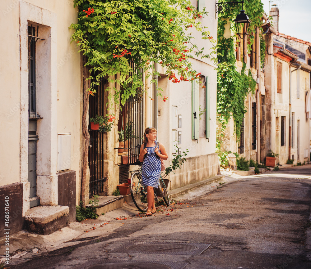 Pretty little girl tourist on the streets of Provence, Wearing blue gingham dress, sunglasses and backpack. Travel with children concept. Image taken in Arles, France