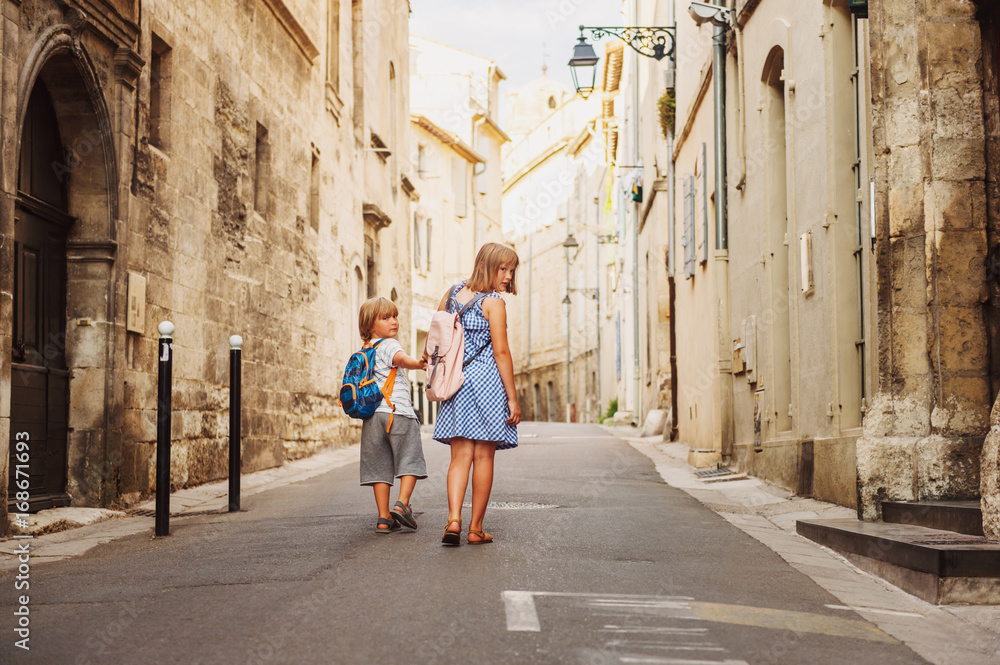 Group of two kids walking on the streets of old european town, wearing backpacks. Travel with children. Back view