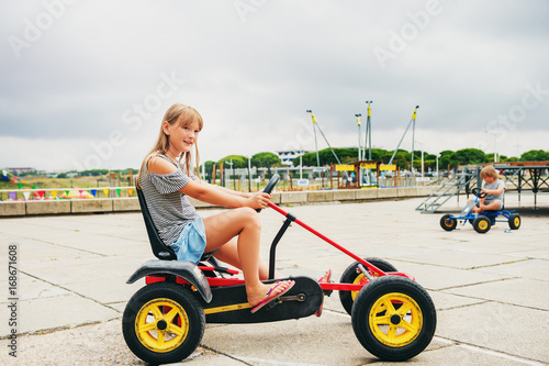 Two active little kids driving pedal race car. Outdoor summer activities for children