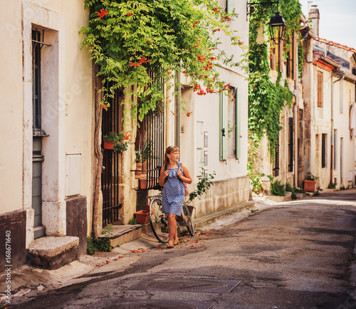 Pretty little girl tourist on the streets of Provence  Wearing blue gingham dress  sunglasses and backpack. Travel with children concept. Image taken in Arles  France