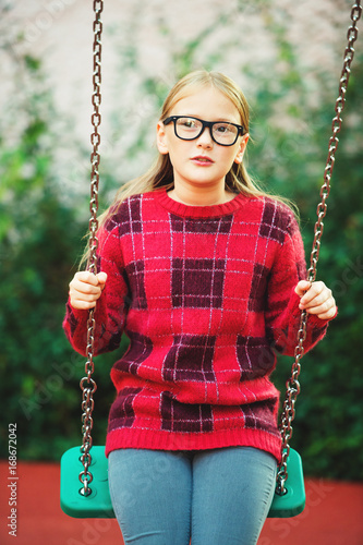 Outdoor portrait of a cute little 9 year old girl wearing eyeglasses and red fashion pullover