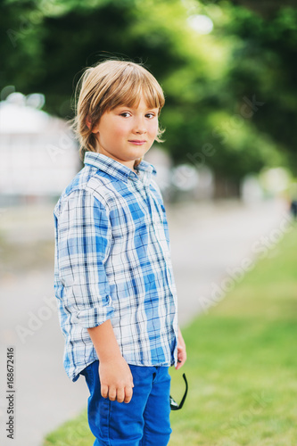 Outdoor fashion portrait of cute little 6 year old boy wearing blue plaid casual shirt and trousers