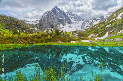 Lake in the mountains of Arkhyz. The beautiful summer landscape with snowy mountain, cloudy sky and lake in the foreground.