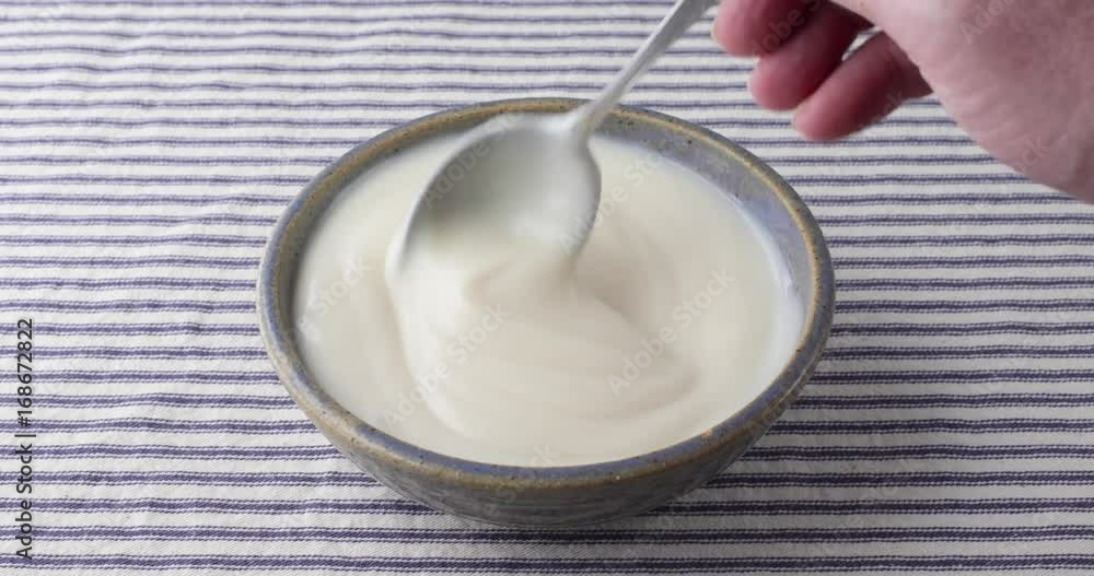 Bowl of vanilla yogurt being stirred with a spoon. Bowl of vanilla yogurt being stirred with a spoon.