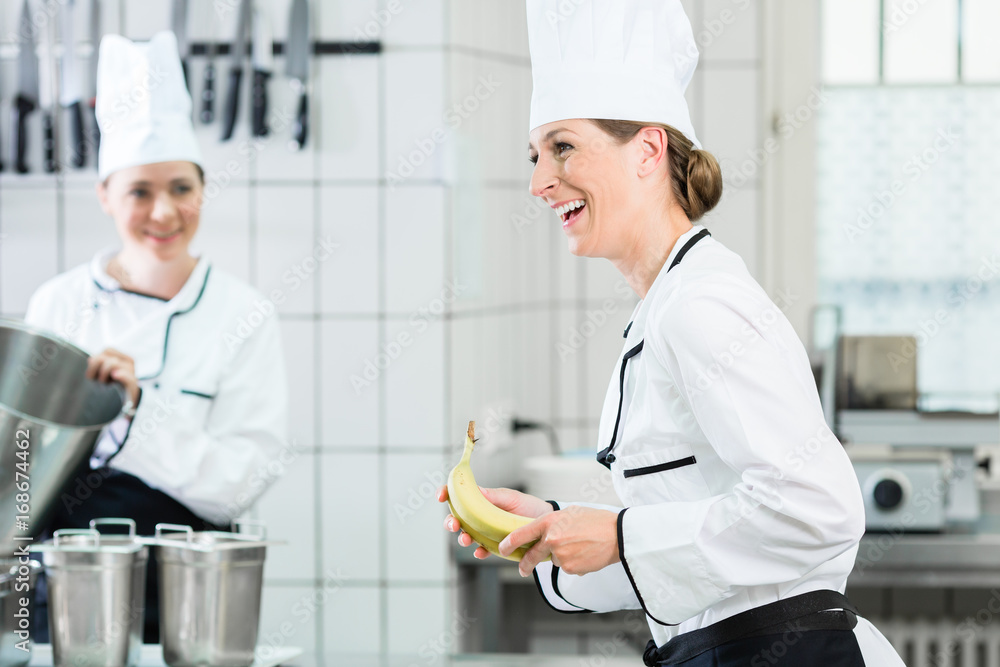 Two female chefs in gastronomic kitchen wearing white cooking uniforms