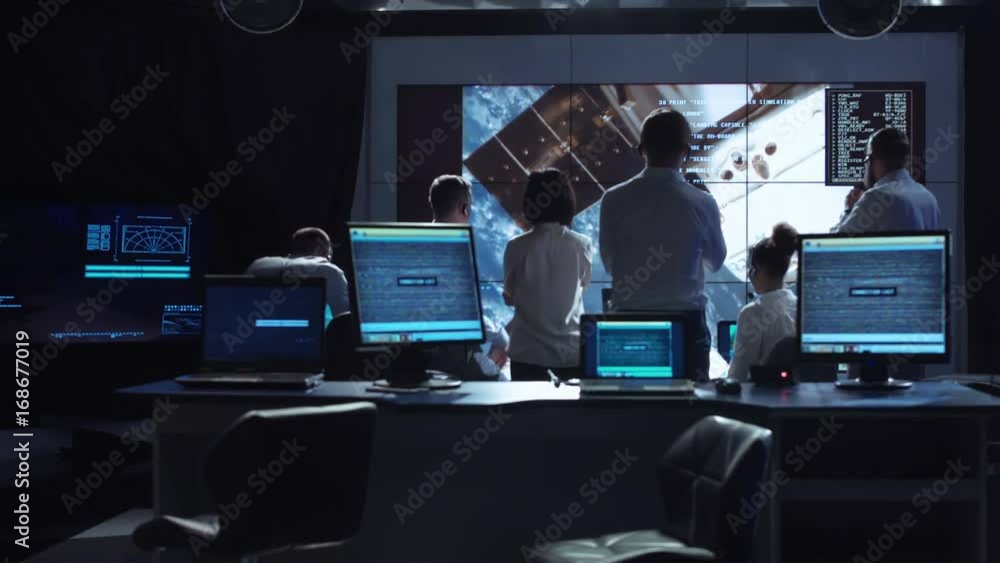 Back view of people working and managing flight in mission control center. Elements of this image furnished by NASA.