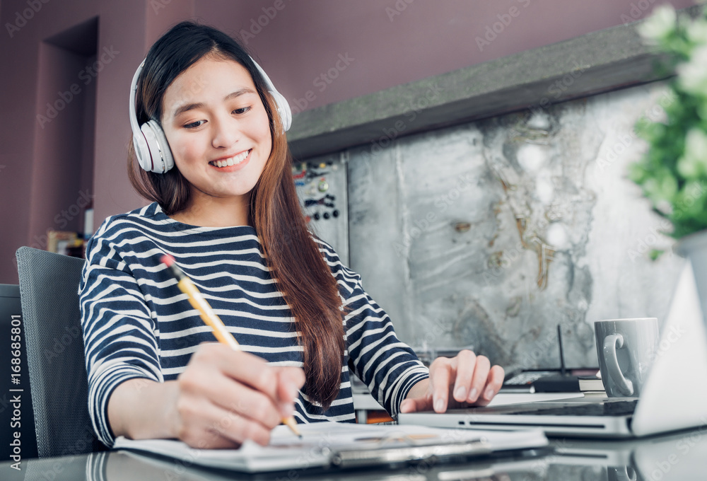 Φωτογραφία Young asian casual businesswoman listening music and writing report on office de
