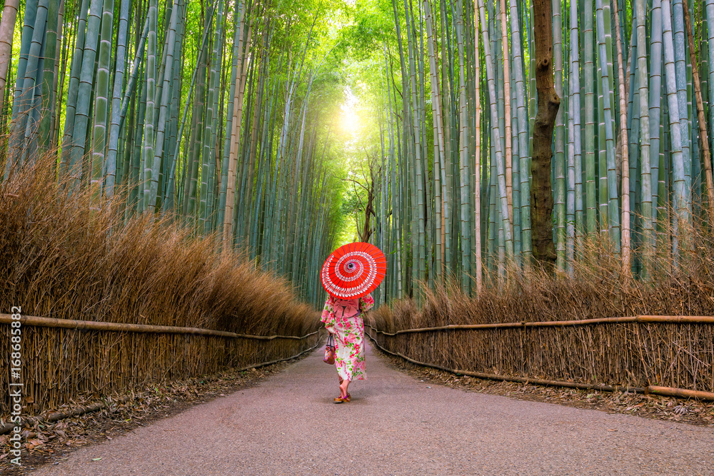 Fototapeta premium Kobieta w tradycyjnym Yukata z czerwonym parasolem przy bambusowym lasem Arashiyama
