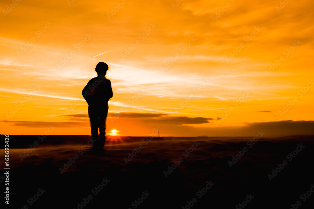 silhouette of young woman standing on the beach sunset.