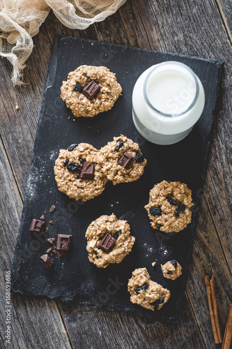 Homemade oatmeal raisin cookies with chocolate and milk on slate background. Selective focus, toned image
