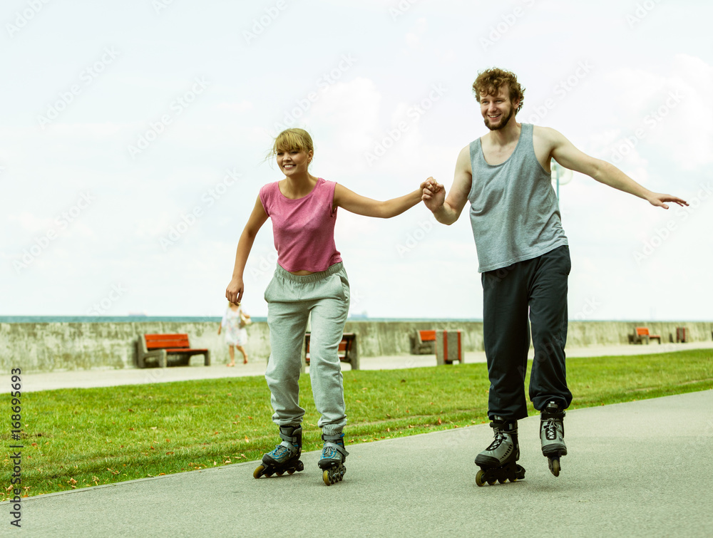Fototapeta premium Young couple rollerblading in park holding hands.