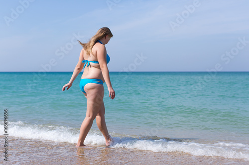 Overweight woman in blue bikini enters the sea water © azazello