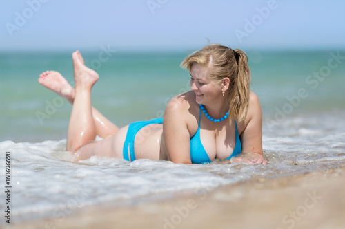 Overweight woman in bikini lying on front in sea foam