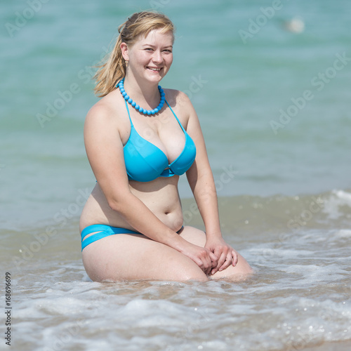 Obraz na plátně Adult woman in bikini sitting in water hands on knees
