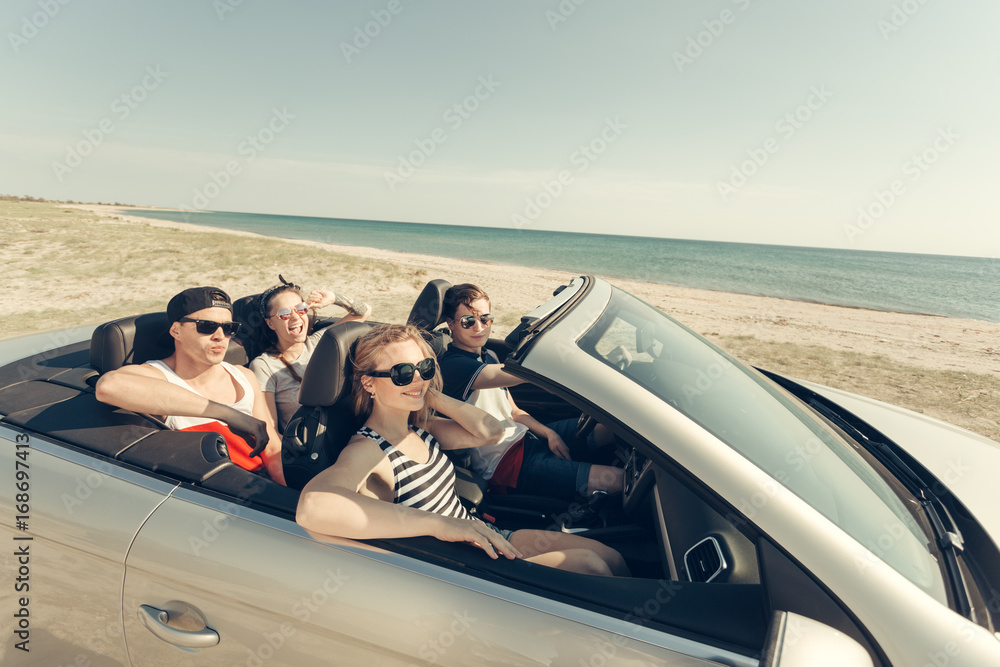 Smiling friends driving car near the sea and having fun