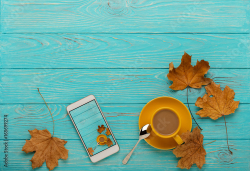 Autumn still life - coffee with leaves and mobile phone with a photo on a blue wooden background.