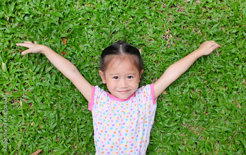Smiling small happy asian girl relaxing on green grass in the park. Smiling small happy asian girl relaxing on green grass in the park.