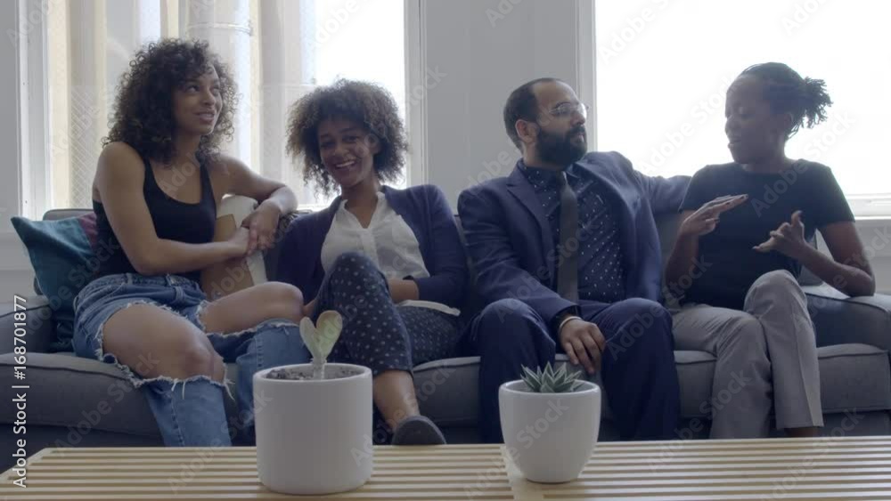 Mixed race group of friends chatting and hanging out on a sofa in a bright, day interior, urban loft or apartment. Slow motion hand-held 4K, recorded at 60fps. Mixed race group of friends chatting and hanging out on a sofa in a bright, day interior, urban loft or apartment. Slow motion hand-held 4K, recorded at 60fps.