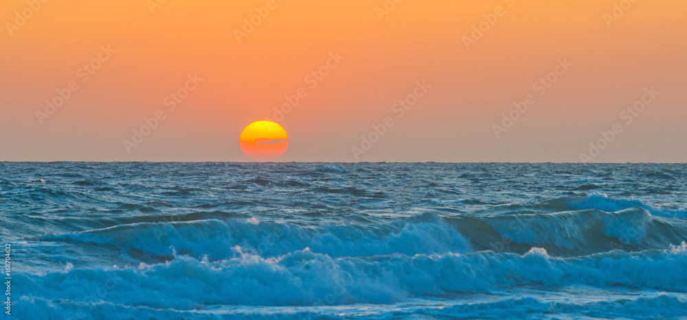 Sea along a sandy beach in the light of sunset in summer