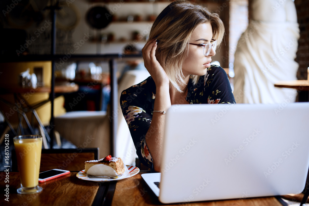 A young attractive woman sitting in a cafe with a laptop. Charming female freelancer thinking about new ideas during work on net-book A young attractive woman sitting in a cafe with a laptop. Charming female freelancer thinking about new ideas during work on net-book