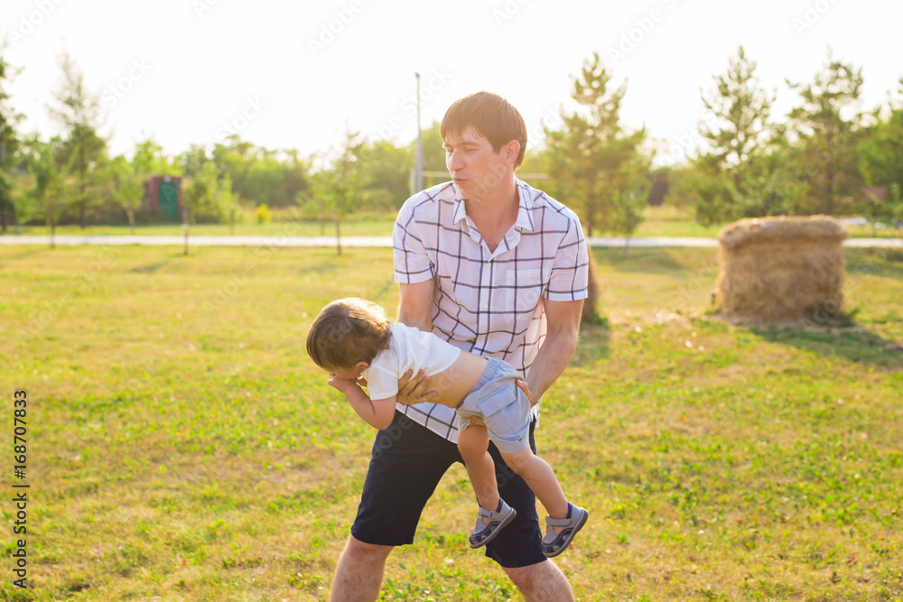 Fototapeta premium Father and son playing on the field at the day time. People having fun outdoors. Concept of friendly family