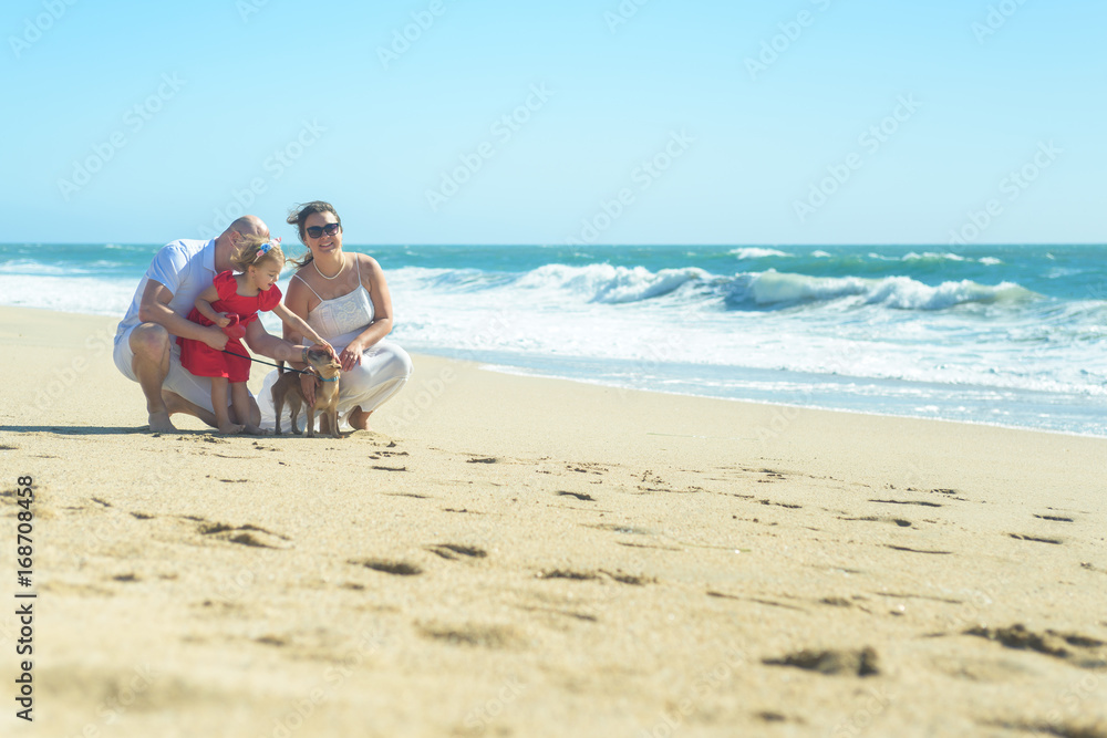 Family with girl in red dress and dog on the beach
