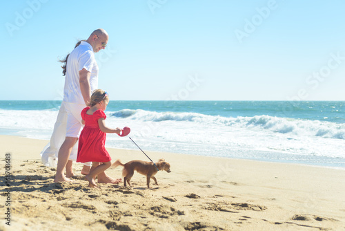 Young family with girl in red dress and dog on the beach