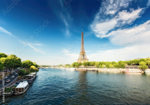 The Eiffel Tower in Paris, France, on a sunny day with the river Seine and dramatic clouds. Colourful travel background. Popular travel destination