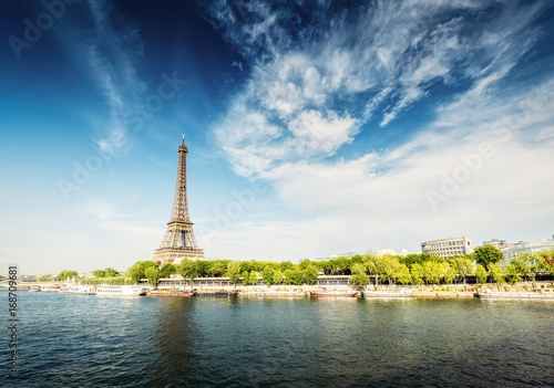 The Eiffel Tower in Paris, France, on a sunny day with the river Seine and dramatic clouds. Colourful travel background. Popular travel destination