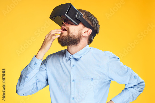 A young guy with a beard on a yellow background in virtual reality glasses