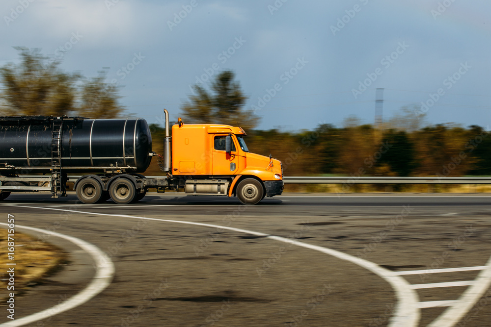 Orange truck with a tank rides on the highway, blurred background