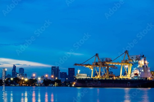Container loading by crane, cargo ship at shipping port at twilight, Logistics and transportation concept © Pawin