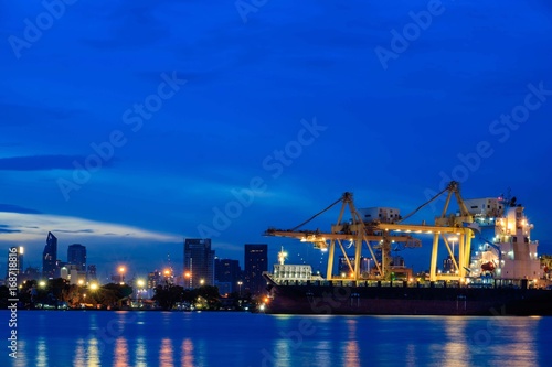 Container loading by crane, cargo ship at shipping port at twilight, Logistics and transportation concept © Pawin