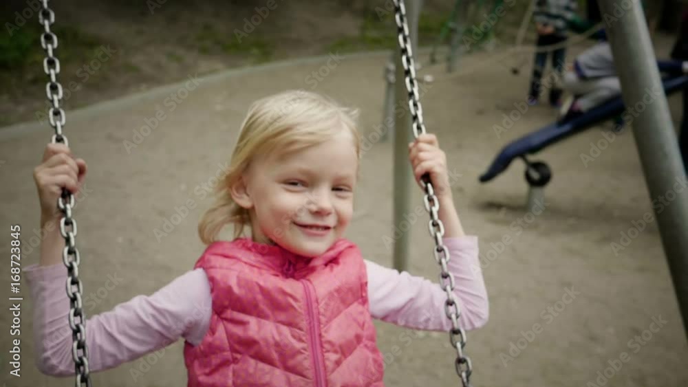 A positive smiling little girl showing her tongue during swinging on a swing at children's playground. Slow Motion. HD A positive smiling little girl showing her tongue during swinging on a swing at children's playground. Slow Motion. HD