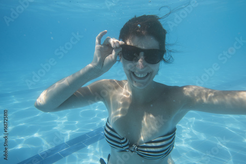 Young dark haired woman underwater smiling with sunglasses