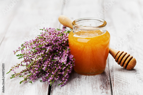 Delicious fresh honey in pot or jar and flowers heather on wooden vintage background.