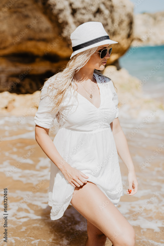Beautiful blonde caucasian woman walking on the beach with cave beach of ocean coast.
