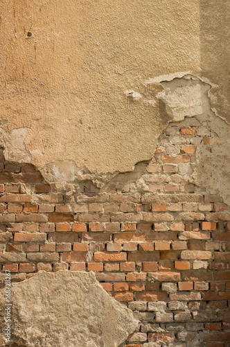 Aged yellow wall with bricks and broken plaster