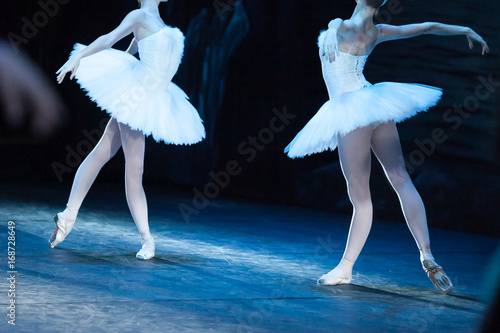choreography, art, ballet concept. impeccable bodies of two female ballet dancers are shinning in bright light of projectors, they are raising their hands like beautiful and majestic swans