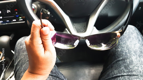 Sun glasses in man hand with brightness of sunlight to the car