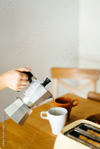 Girl hands close up pouring coffee in a Cup on a wooden table in the morning.