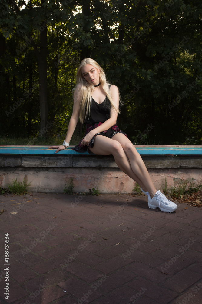  Lovely young model with long blonde hair  posing on a bench in the park
