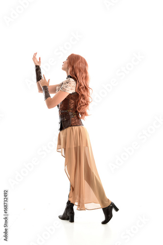 full length portrait of a red haired lady wearing steampunk inspired outfit, standing pose against a white background.