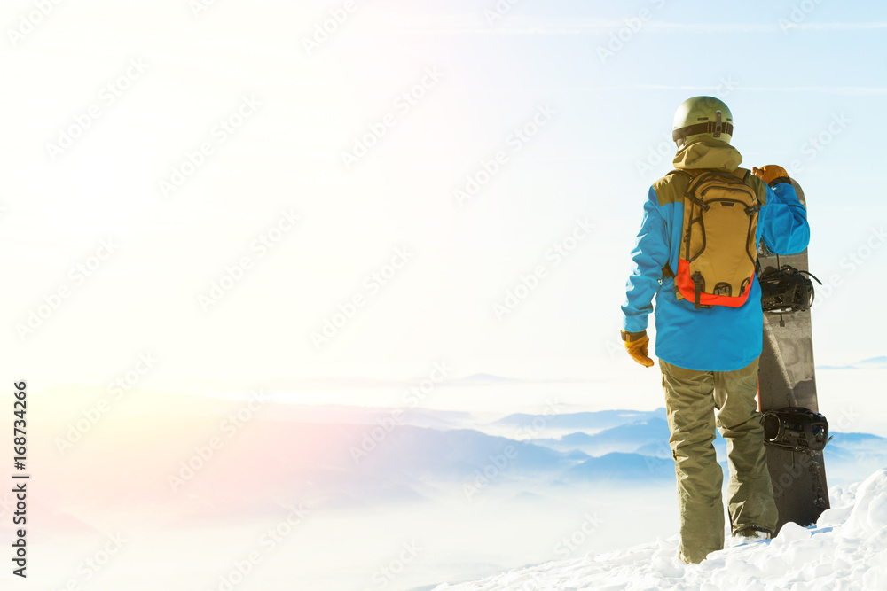 Young snowboarder in helmet standing next to snowboard thrusted into snow with beautiful scenery on background Young snowboarder in helmet standing next to snowboard thrusted into snow with beautiful scenery on background
