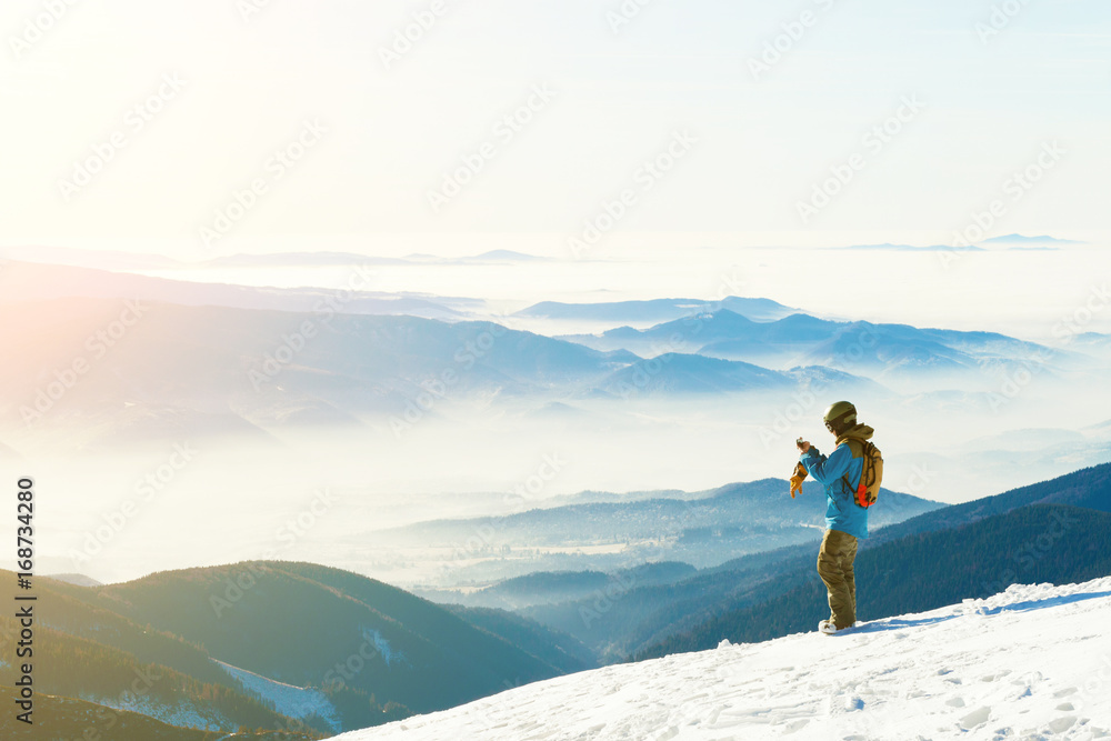 Male snowboarder taking photo of the beautiful landscape from the very top of a mountain