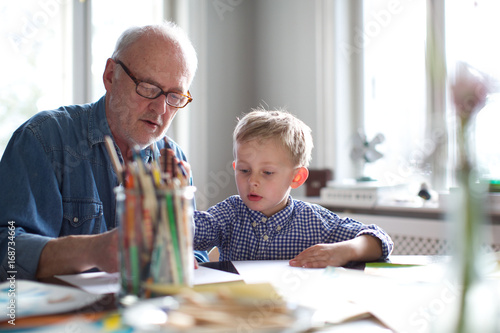 grandfather helping grandson with homework. concentration, kindergarten teacher, glasses, study. photo