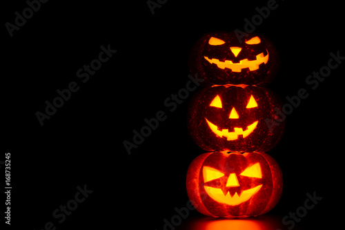 Three spooky carved pumpkins on table in darkness